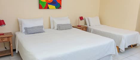 A hotel room with two single beds, a wooden nightstand with a red lamp, and a colorful abstract painting on the wall.