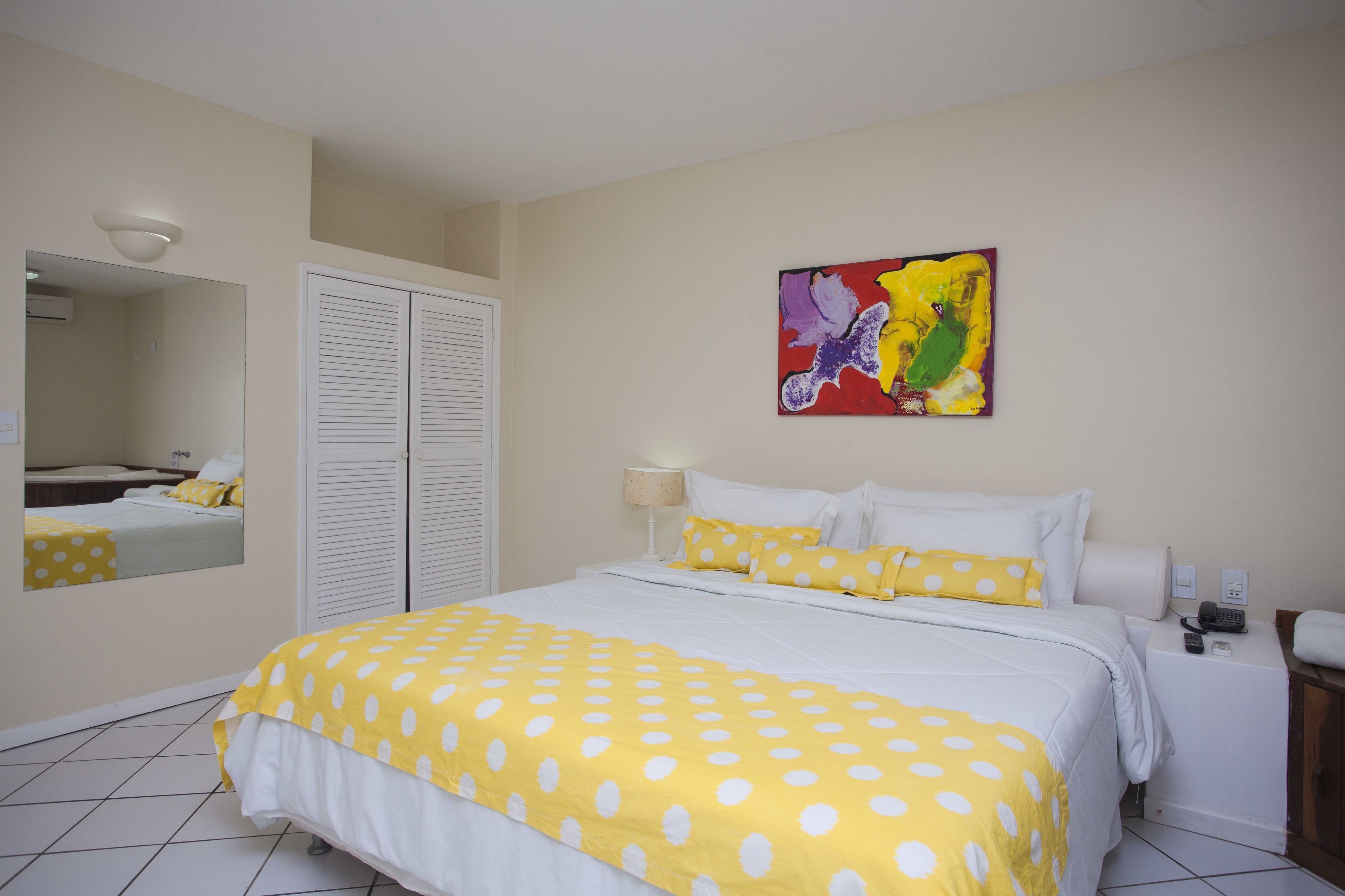 A hotel room with a bed, a bedside table with a lamp, a phone, and a painting on the wall.