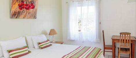 Et hotelværelse med en seng, et skrivebord, en stol, en lampe og et billede på væggen.