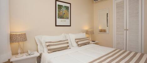 A bedroom with a bed, nightstands, a lamp, a framed picture on the wall, and a wardrobe.