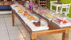 A buffet table with various food items covered in clear plastic containers. - Pousada Dos Reis (Búzios)