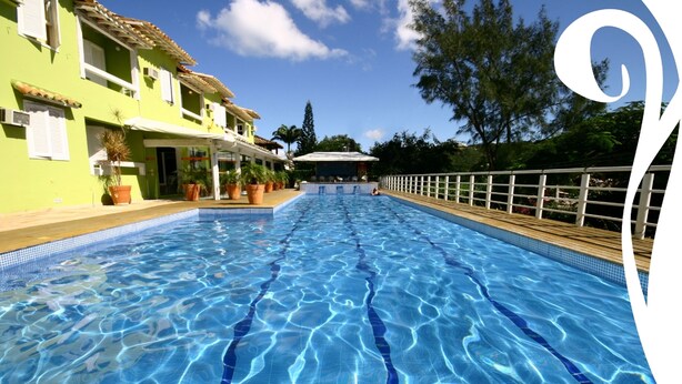 A swimming pool with clear blue water, surrounded by a wooden deck and a white fence. - Pousada Dos Reis (Búzios)