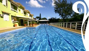 A swimming pool with clear blue water, surrounded by a wooden deck and a white fence. - Pousada Dos Reis (Búzios)