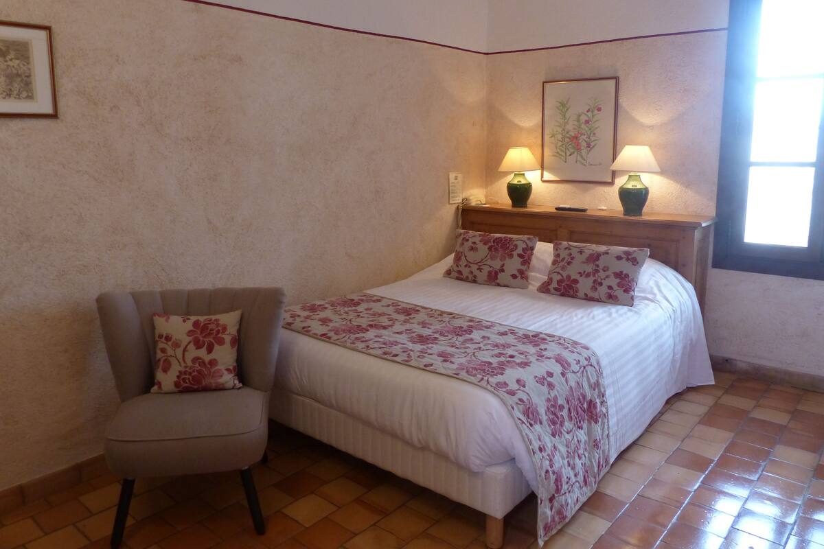 A bedroom with a bed, a chair, a nightstand with lamps, and a window.