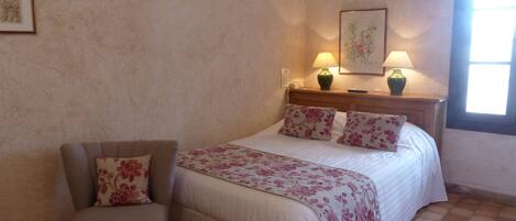 A bedroom with a bed, a chair, a nightstand with lamps, and a window.