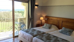 A hotel room with two beds, a balcony with a view, a small table, and a lamp. - Hotel Charembeau (Forcalquier)