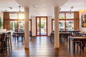 A spacious indoor dining area with multiple tables and chairs, large windows, and a view of the outdoors.