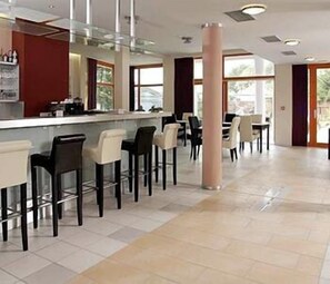A modern bar area with high stools and a counter, large windows, and a tiled floor. - U Pramenu (Plzen)