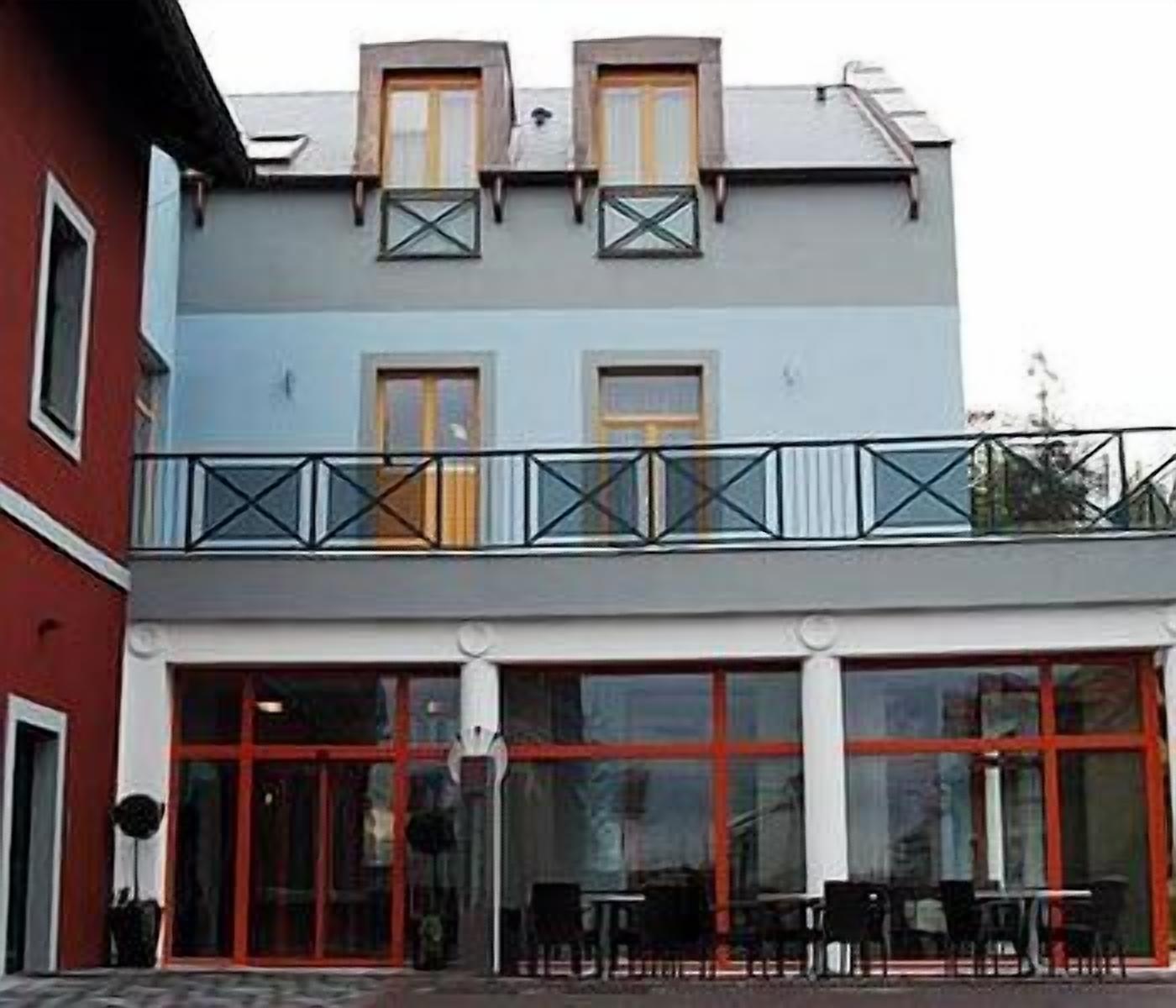 Ein zweistöckiges Gebäude mit Balkon, großen Fenstern und einer roter Tür.