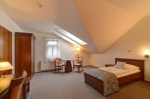 A hotel room with a bed, a desk, a chair, a table, and a window with curtains.