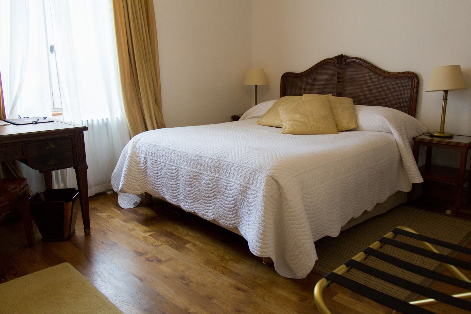 Una cama bien hecha con colcha blanca, dos lámparas de noche y un cabecero de madera.