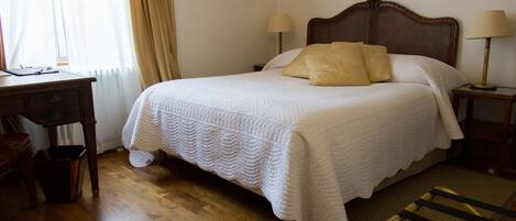 Una cama bien hecha con colcha blanca, dos lámparas de noche y un cabecero de madera.