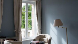 Une pièce dotée d’une grande fenêtre, d’un lustre, d’une table ronde et de deux fauteuils.