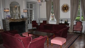 Un salon élégant avec une cheminée, des canapés en velours rouge, une table basse et un tapis à motifs.