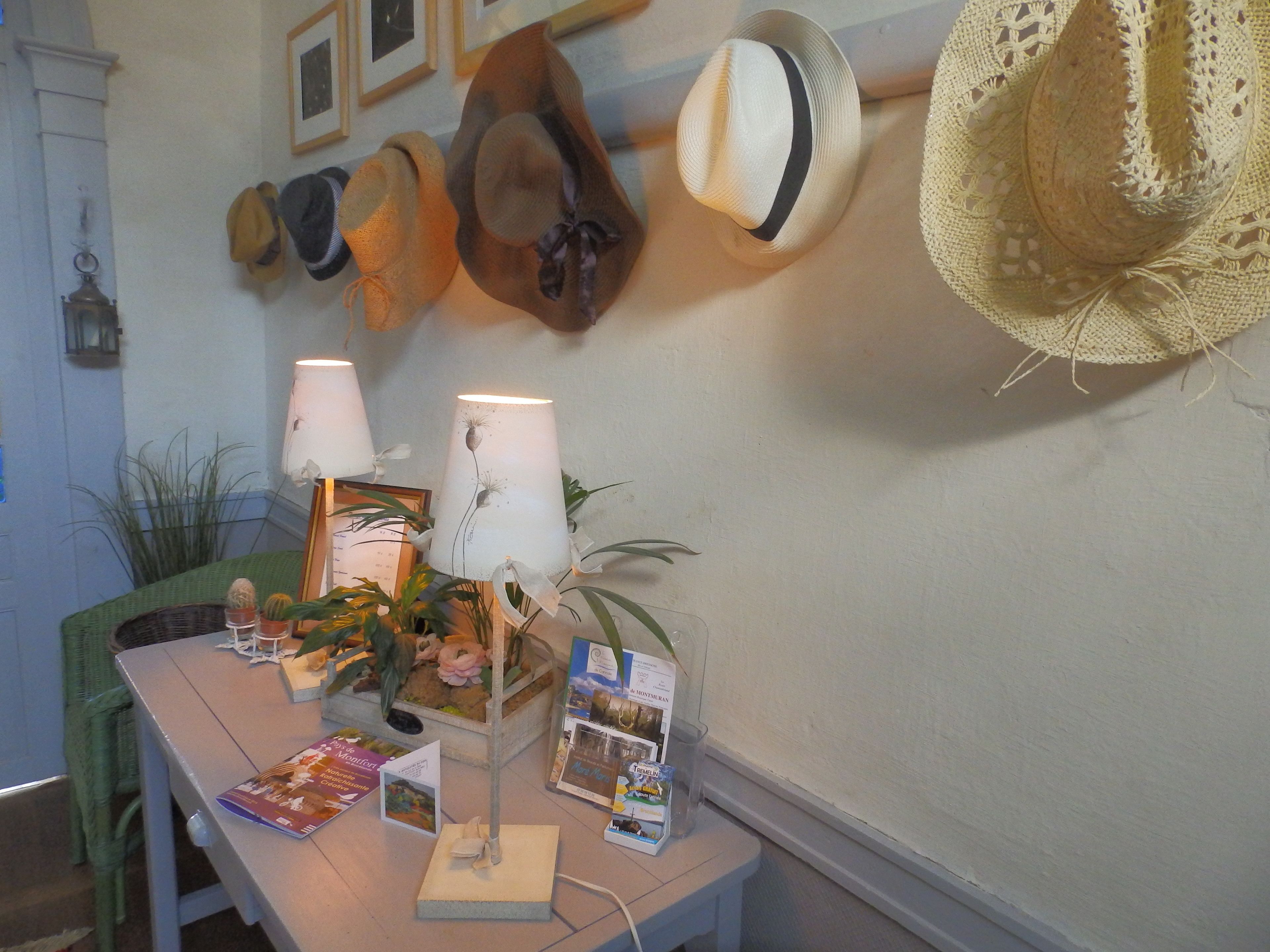 A room with a table displaying hats, a lamp, and some books.