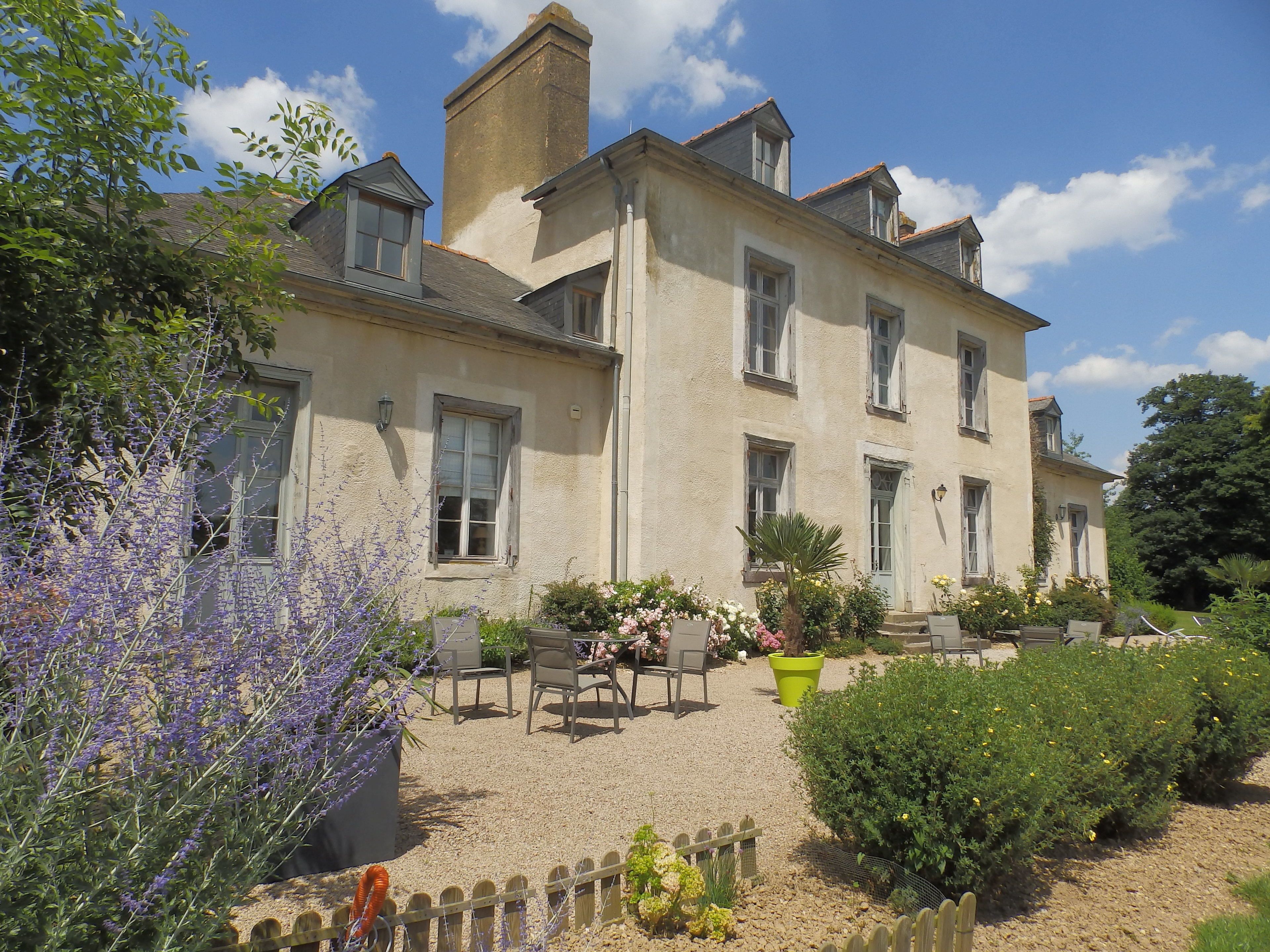 Un grand bâtiment à deux étages, doté de nombreuses fenêtres et d’un espace jardin aménagé avec des sièges extérieurs.