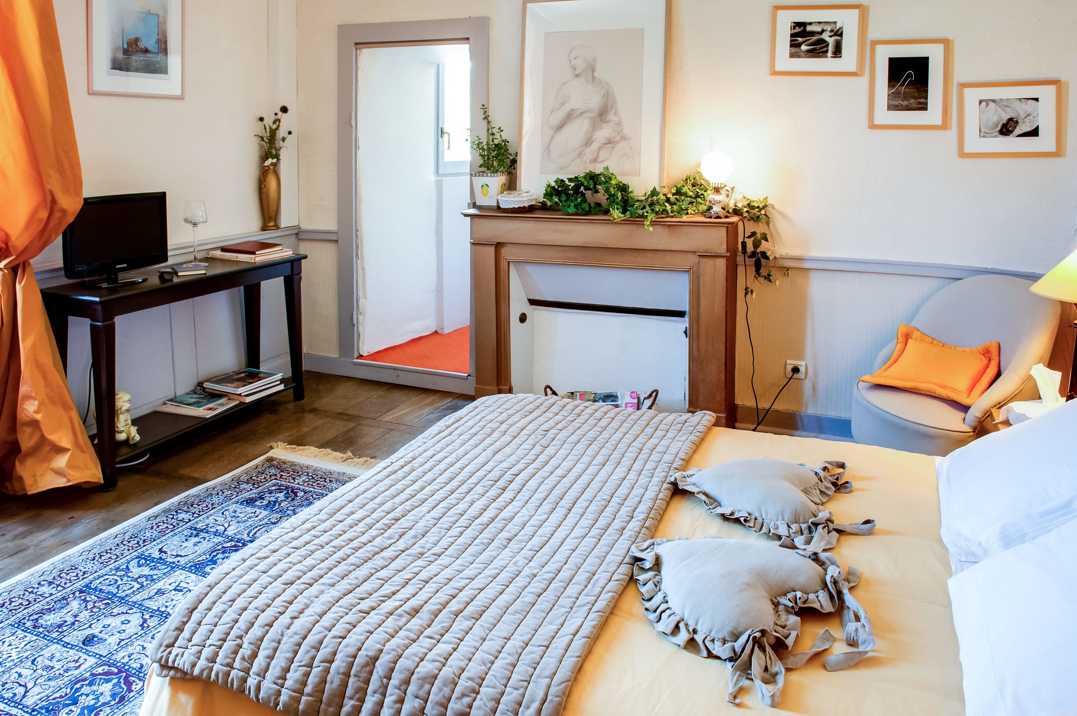 Een hotelkamer met een bed, een bureau met een televisie, een open haard en ingelijste foto’s aan de muur.