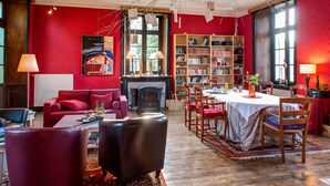 A cozy living room with a fireplace, red walls, and a bookshelf. - Château du Pin (Iffendic)