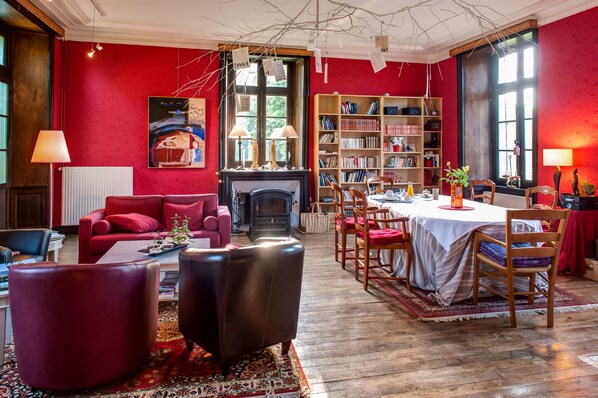 Un salon chaleureux avec une cheminée, des murs rouges et une bibliothèque.