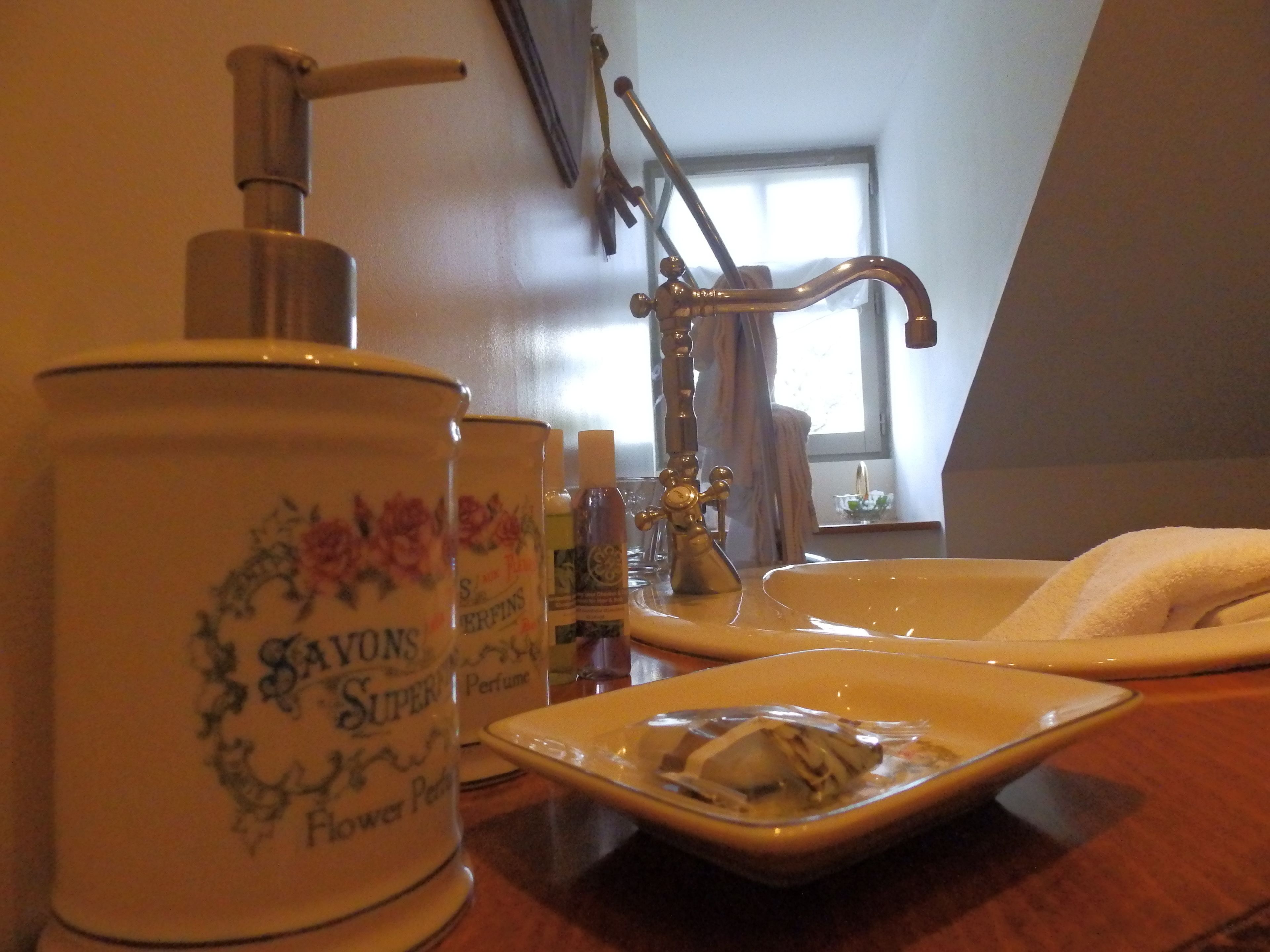 A bathroom with a white sink, a mirror, and a bottle of perfume.