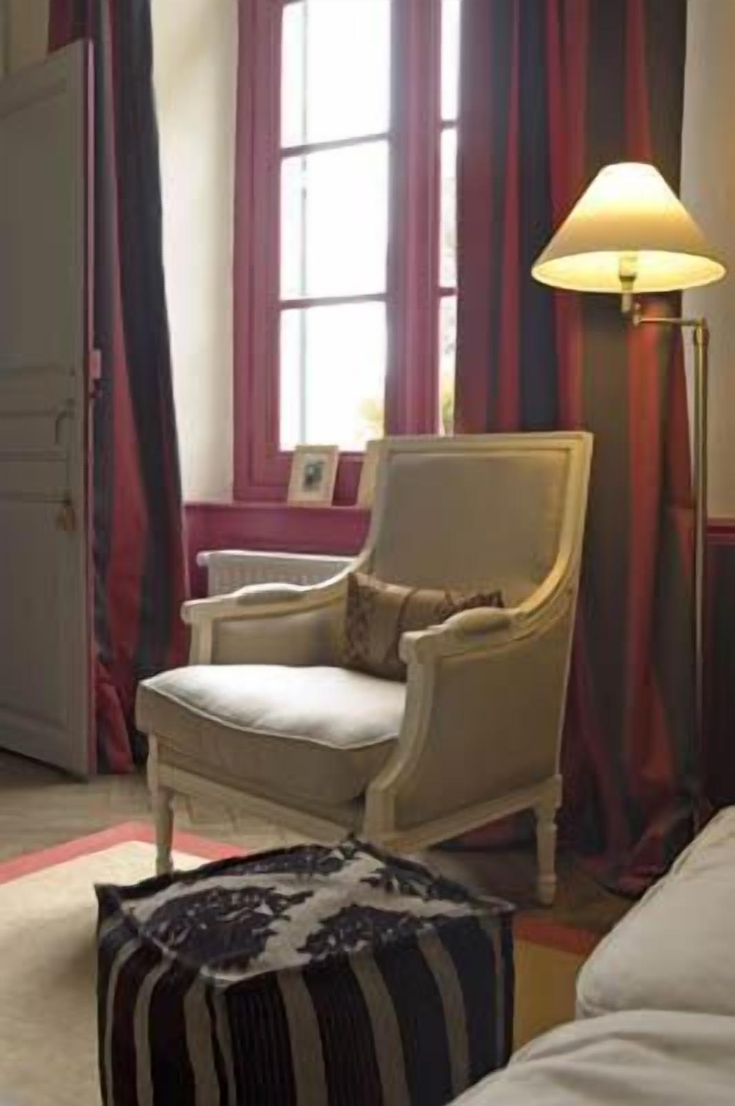 Una habitación con un sillón beige, una lámpara de pie y un reposapiés a rayas.