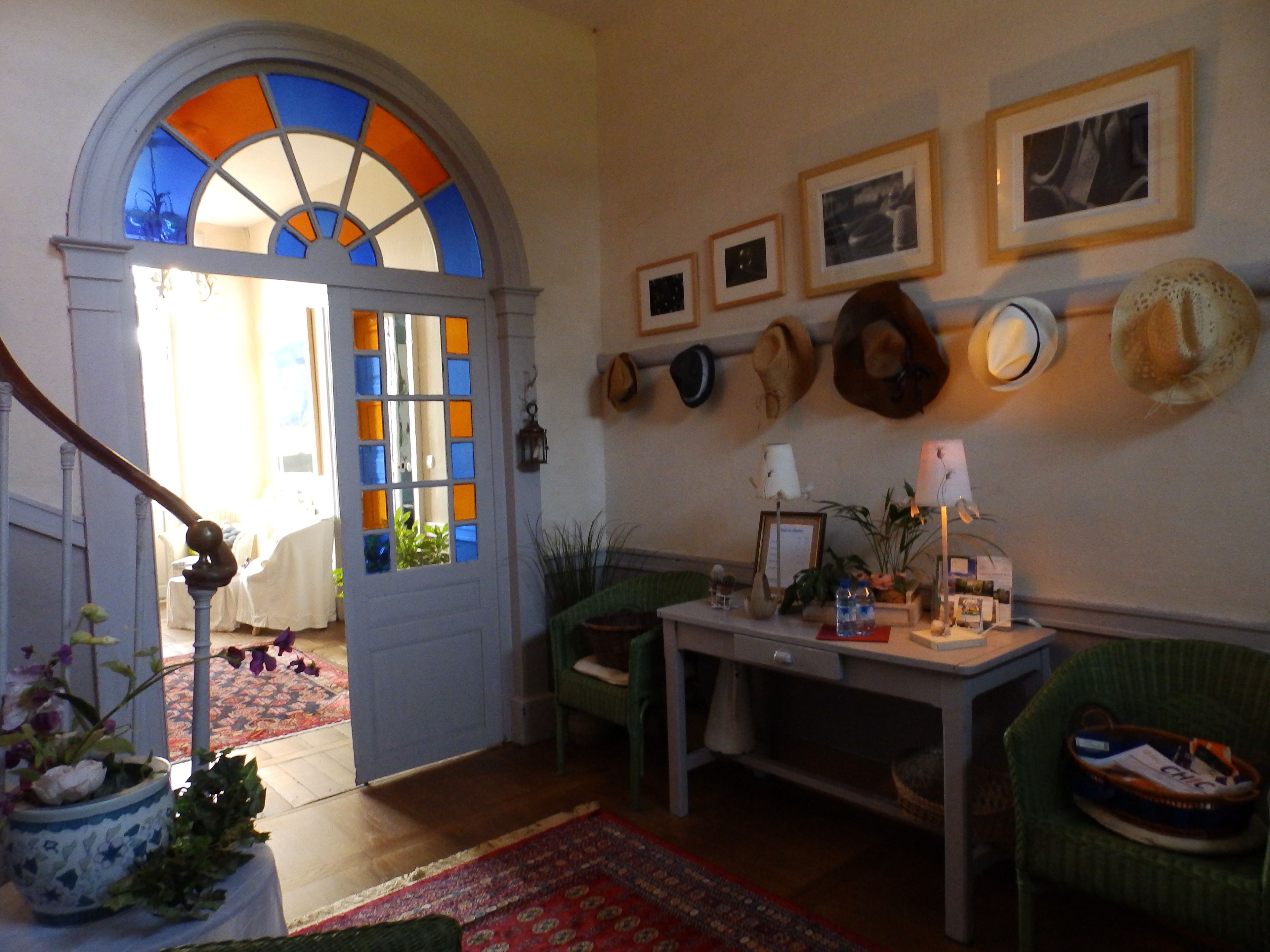 A room with a wooden staircase, a door with stained glass, a table with a vase, and a wall with hats.