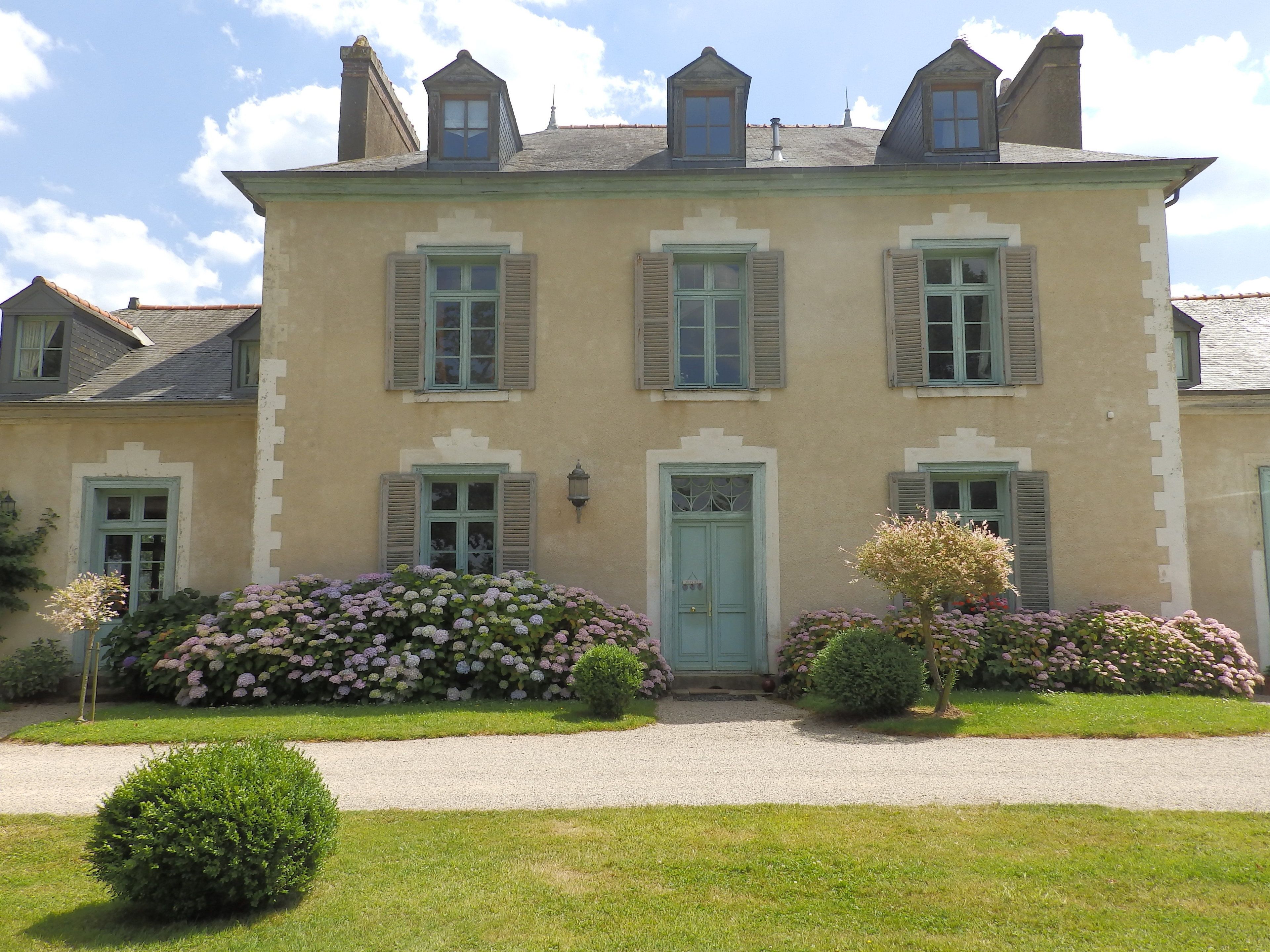 A two-story building with a symmetrical facade, multiple windows with shutters, and a central entrance door.