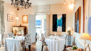 A dining area with tables set for four, a chandelier, and artwork on the walls. - Château du Pin (Iffendic)