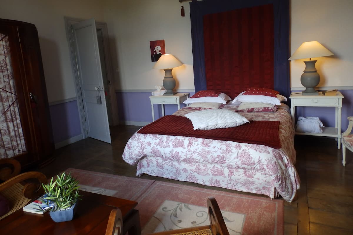 Une chambre à coucher avec un lit, deux tables de chevet avec des lampes, un rideau rouge et une porte.