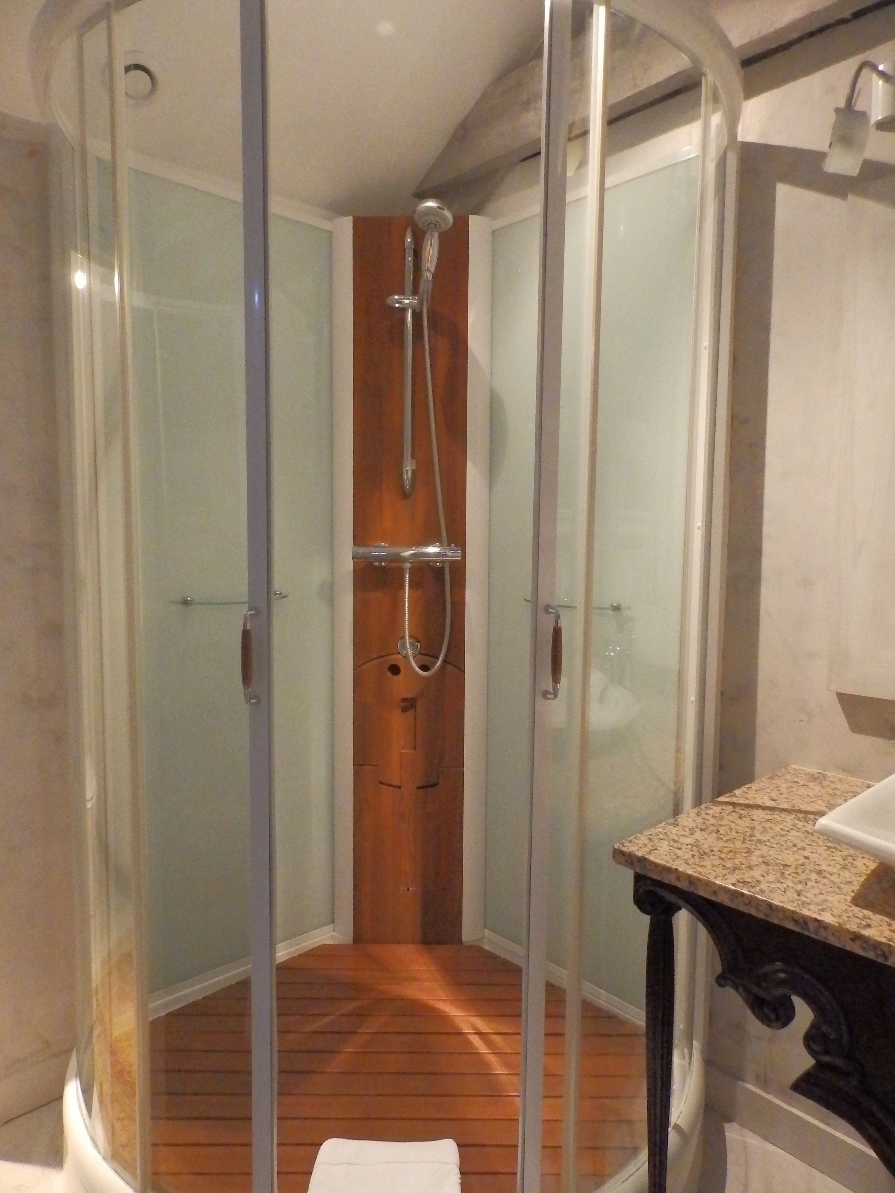 A glass-enclosed shower with a wooden door, a sink with a granite countertop, and a wooden floor.