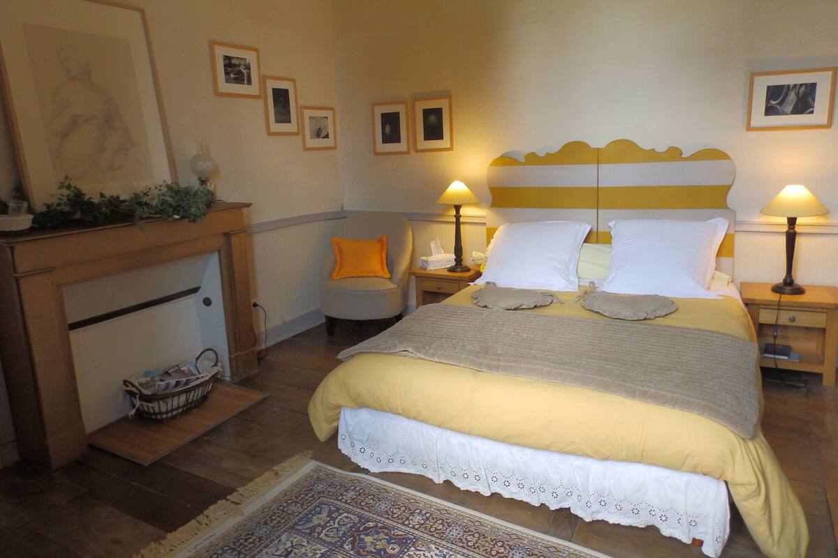 Une chambre bien rangée, avec un lit, des tables de chevet, une chaise et des tableaux encadrés accrochés au mur.