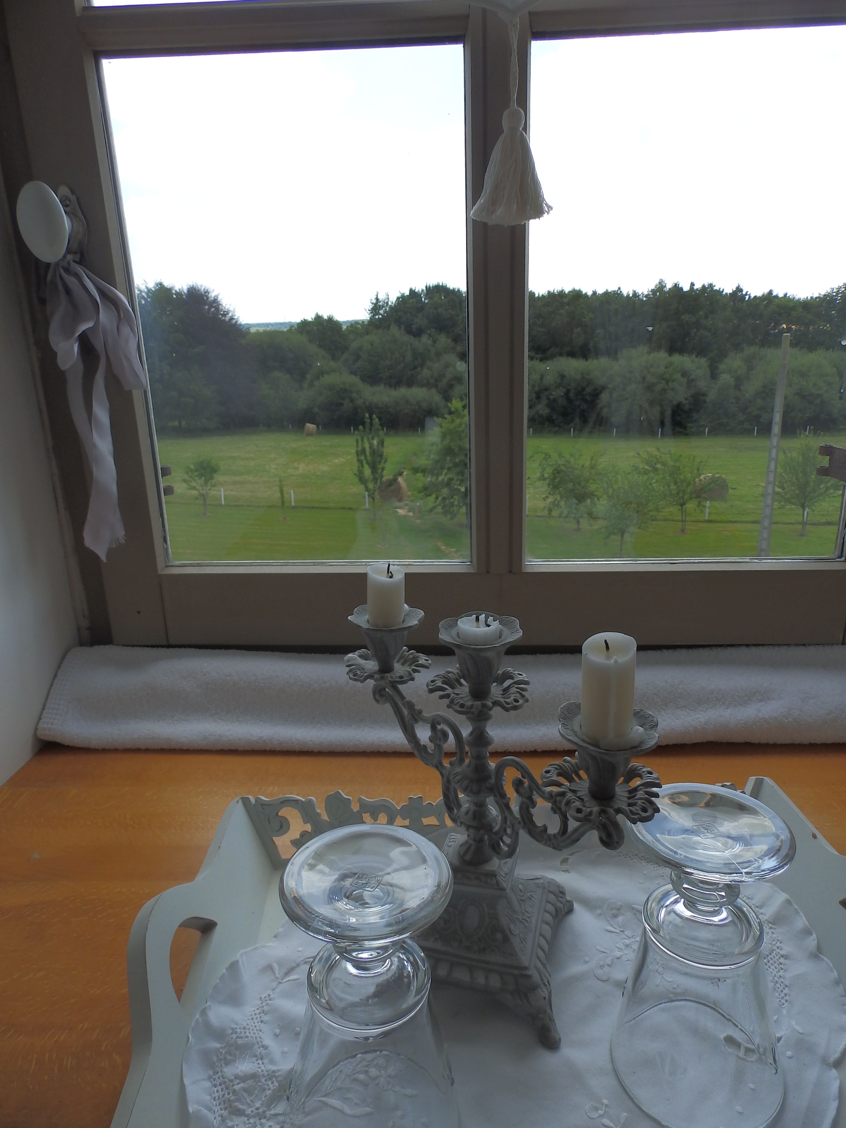 A table with a white tablecloth, a decorative candelabra with candles, and a view of a green landscape through a window.