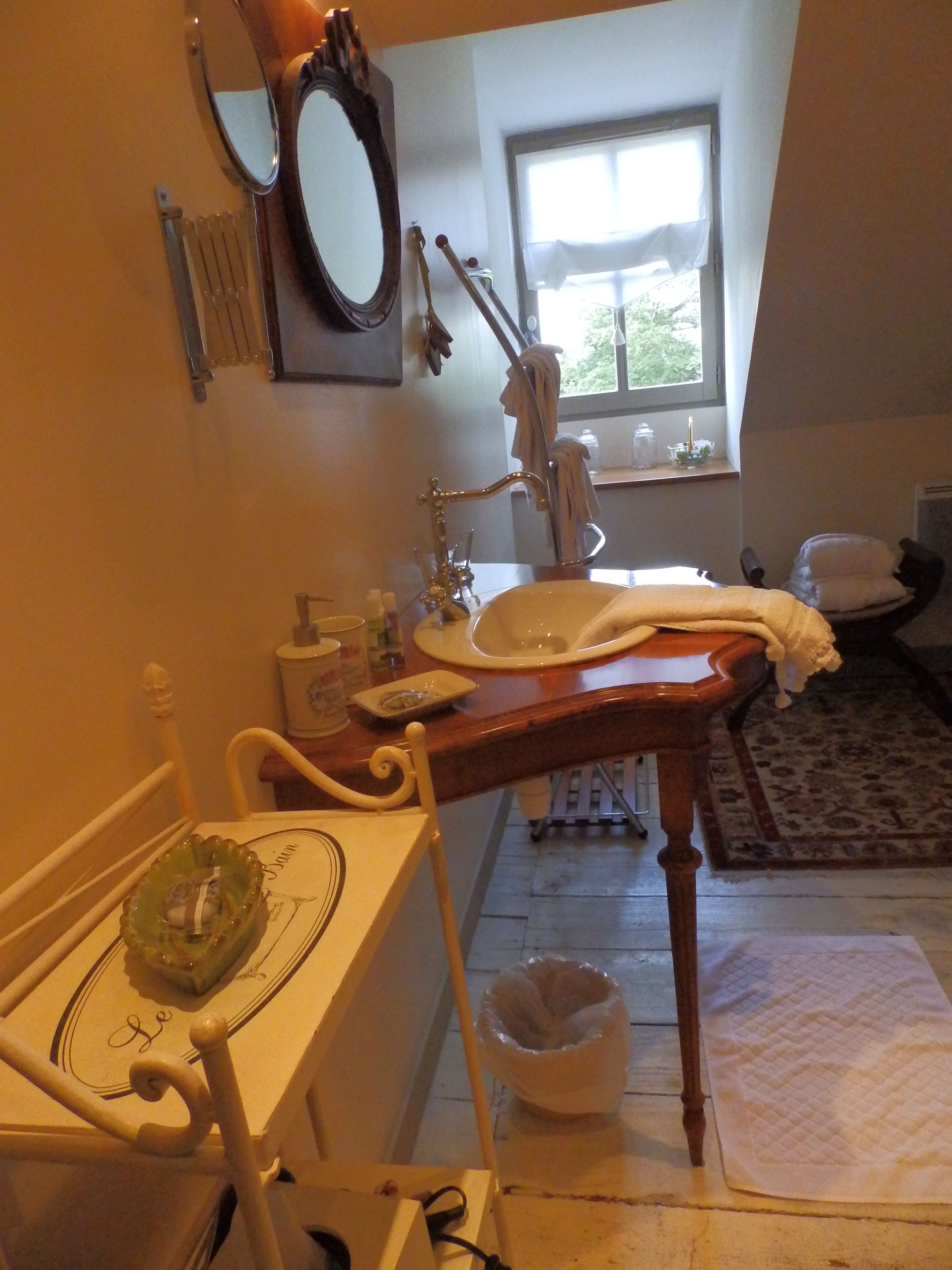Un baño con lavamanos, espejo y ventana. Hay una silla y una alfombra en la habitación.
