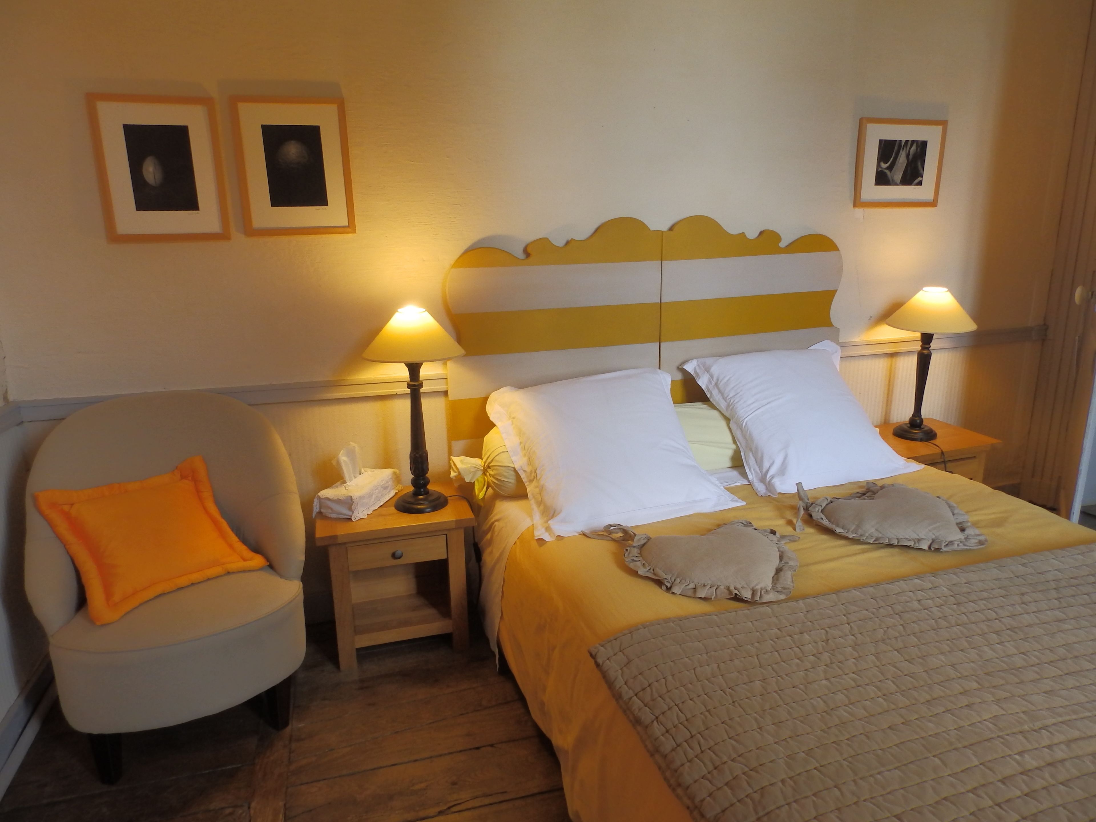A hotel room with a bed, two bedside lamps, a chair, and two framed pictures on the wall.
