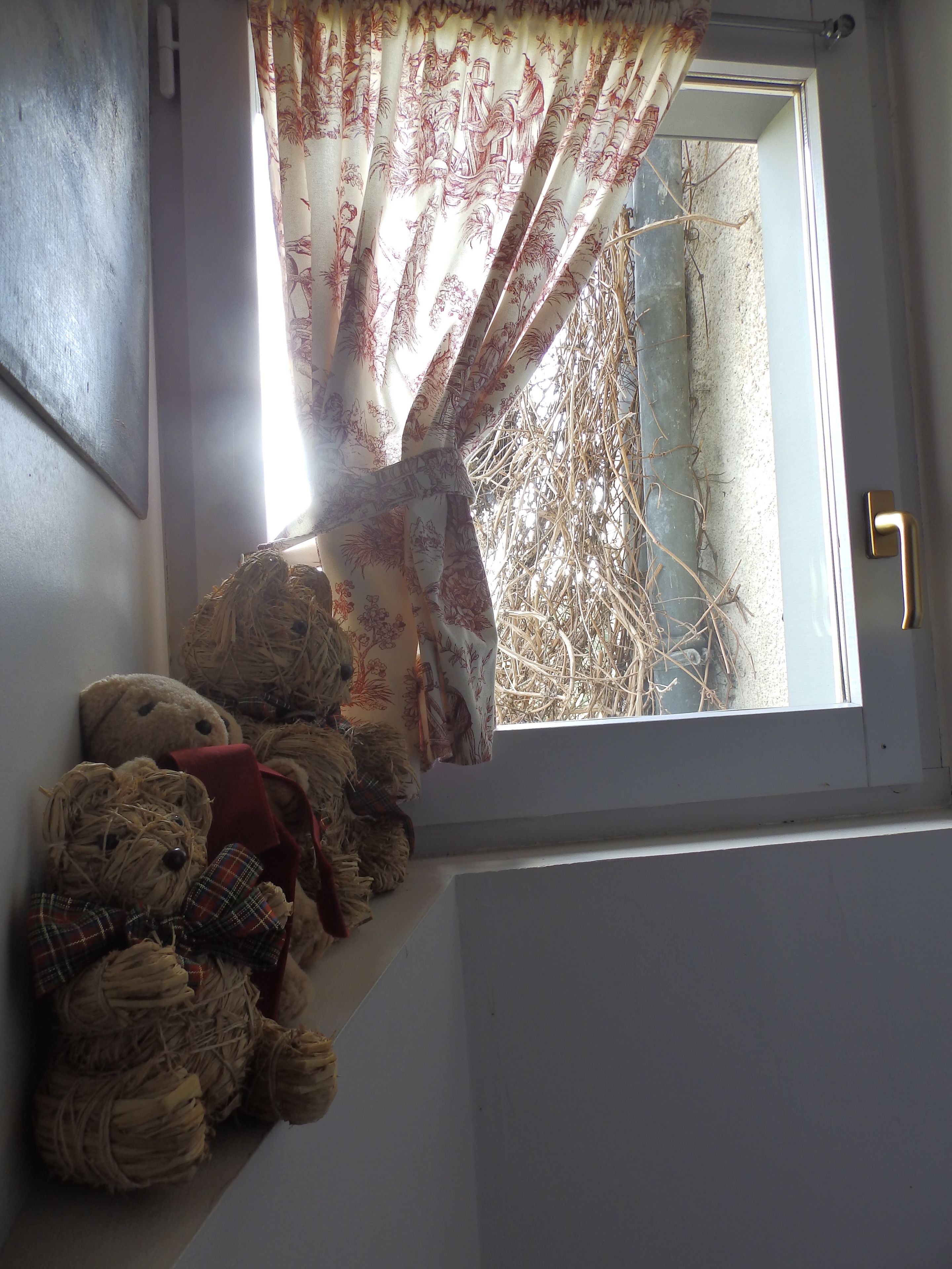 A window with a floral curtain, a teddy bear, and a door with a brass handle.