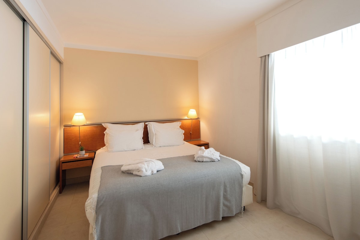 Une chambre d’hôtel avec un lit, deux lampes de chevet, une table de chevet et une fenêtre avec des rideaux.