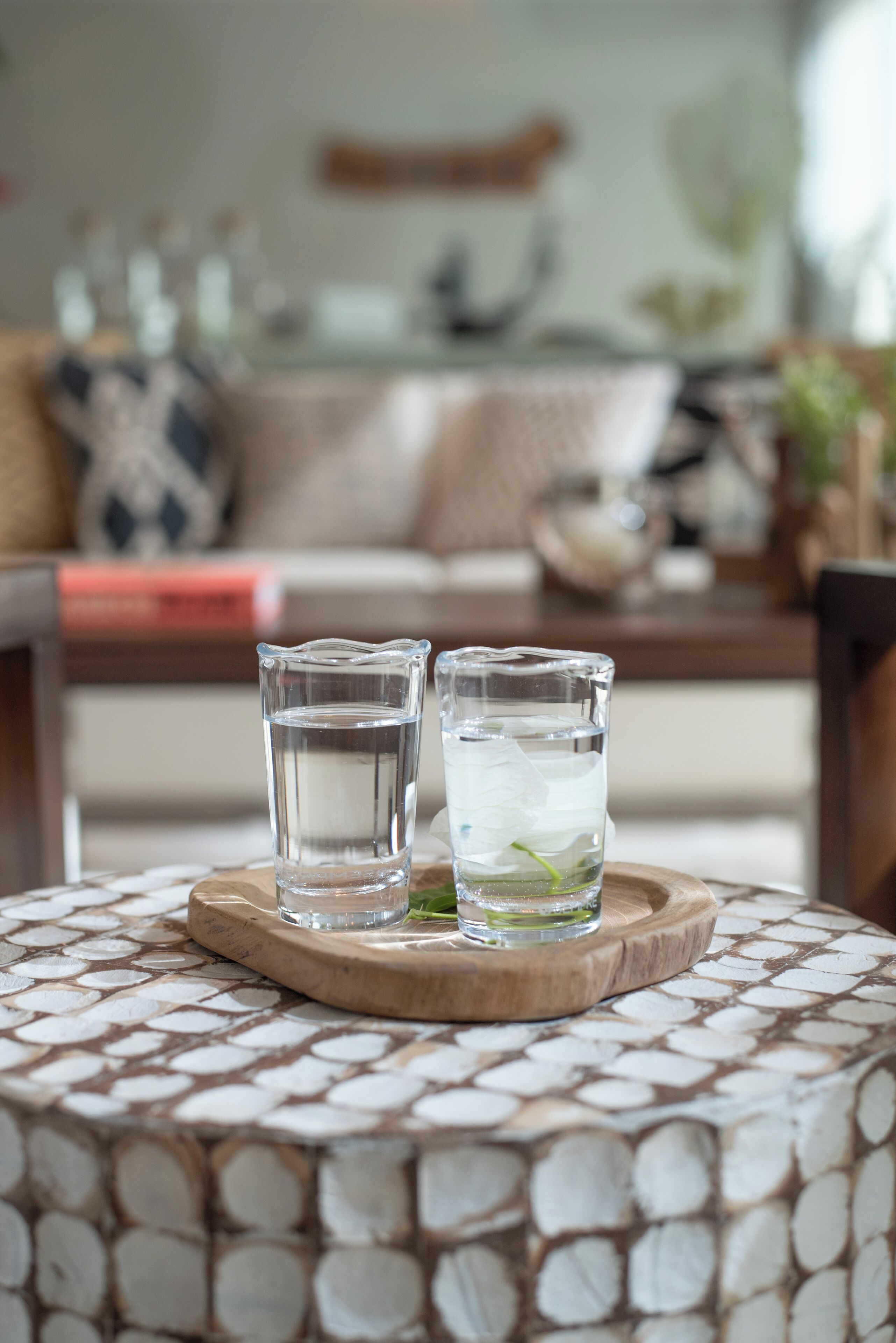 Two glasses of water on a wooden tray on a patterned table.