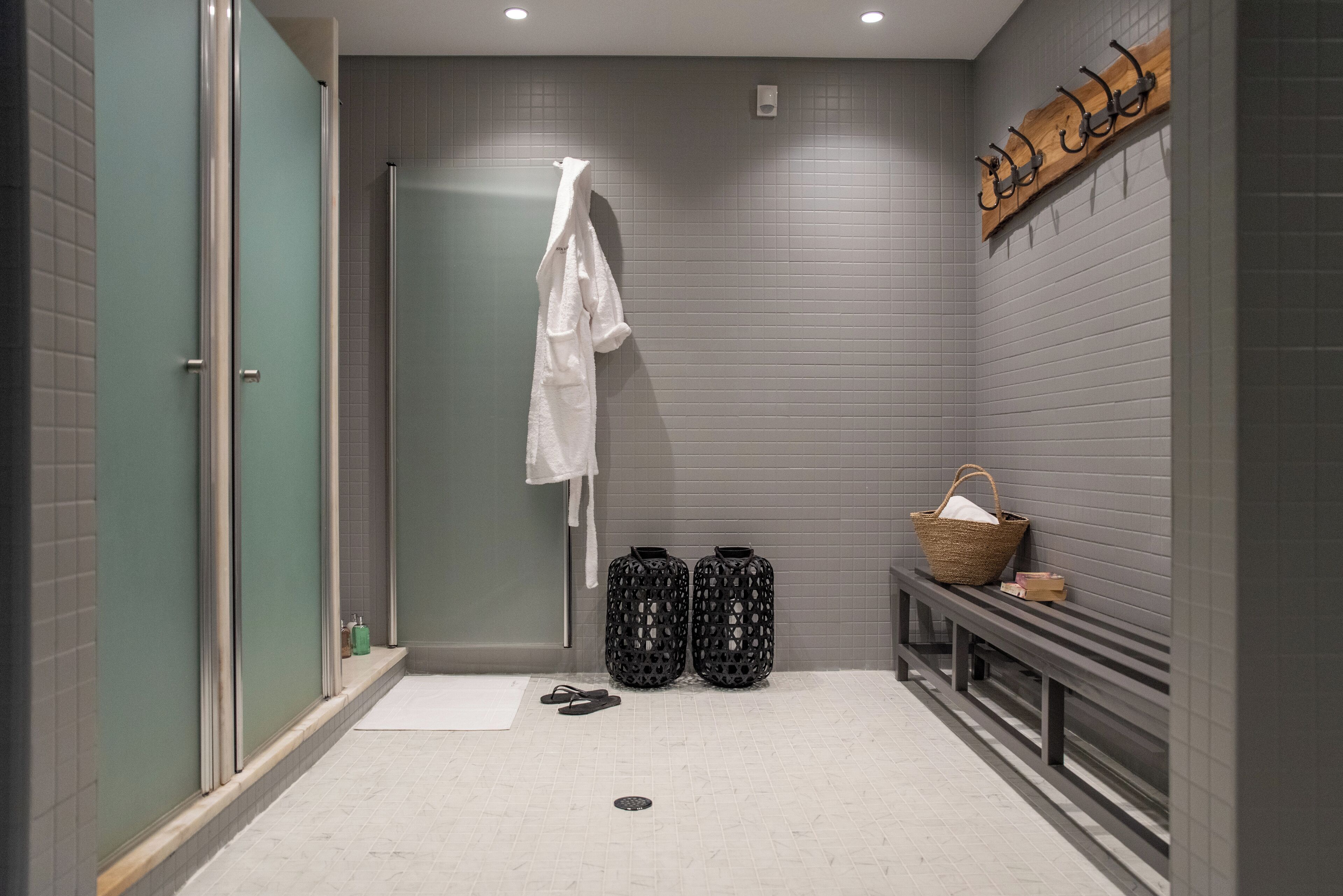 A modern bathroom with a glass shower enclosure, a bench with a basket, and a towel rack.