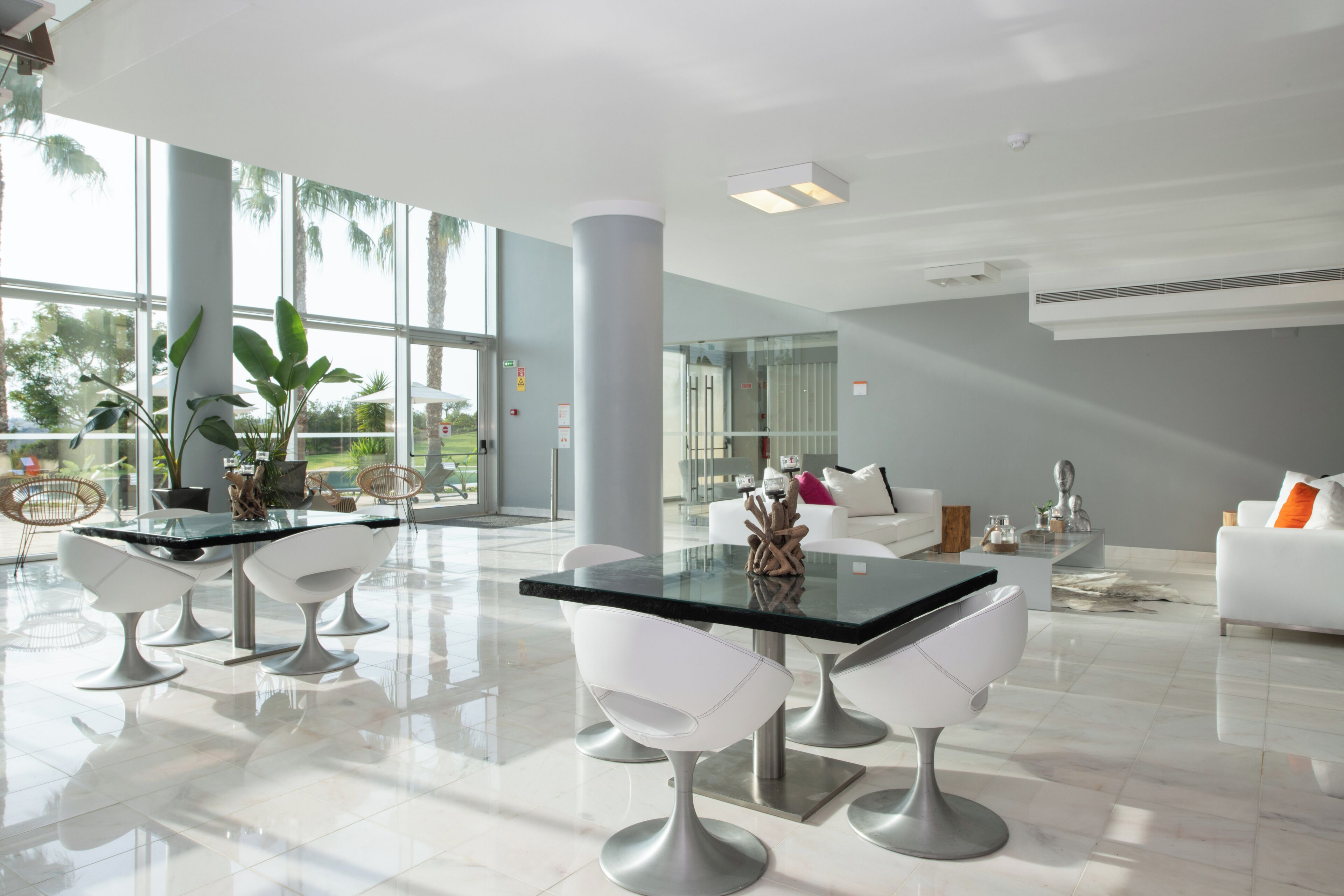 A modern, spacious dining area with a glass table and white chairs, large windows, and a view of palm trees.