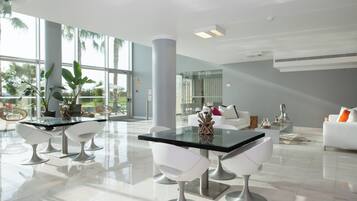 A modern, spacious dining area with a glass table and white chairs, large windows, and a view of palm trees.