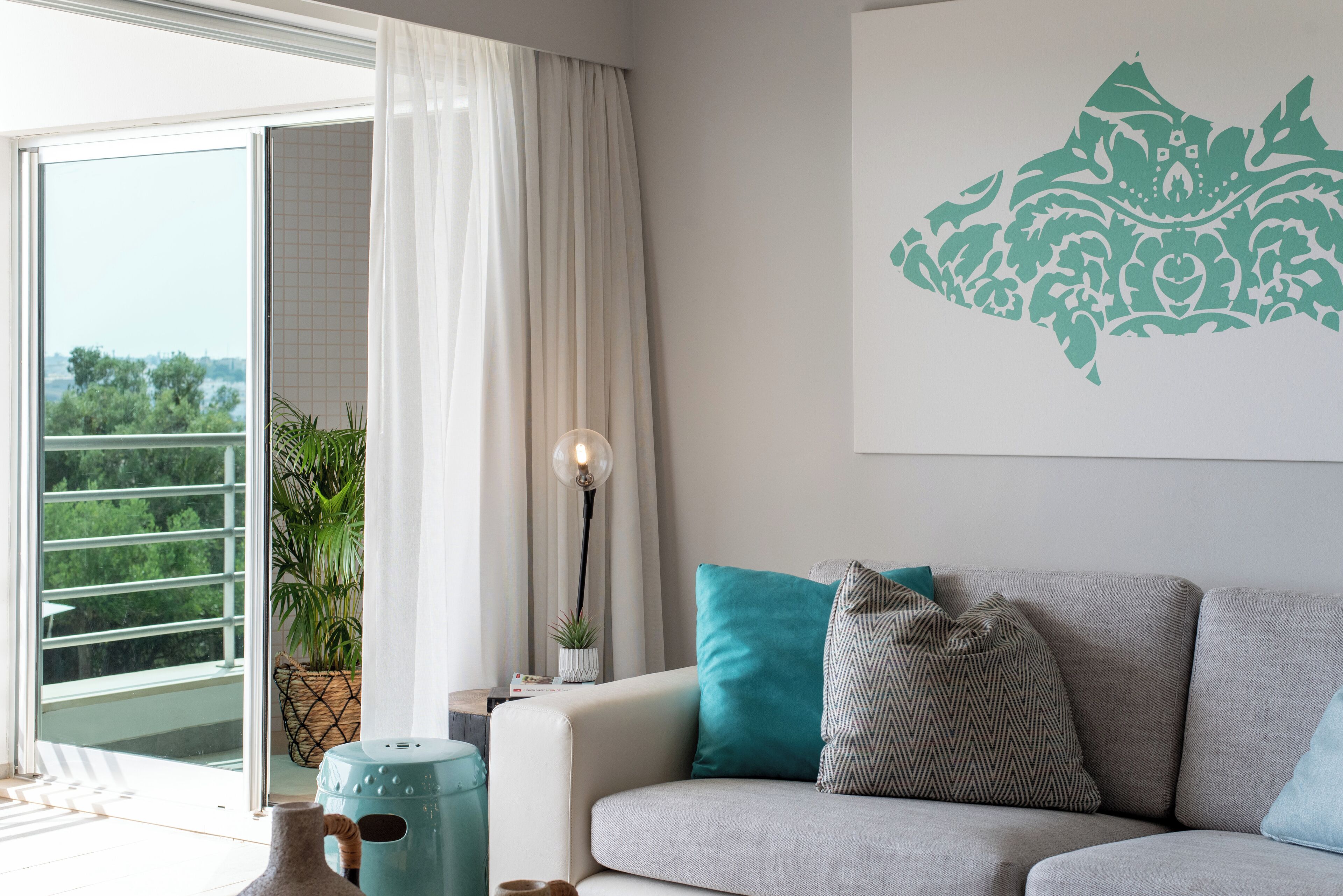 A modern living room with a grey sofa, teal and patterned cushions, a potted plant, and a wall-mounted artwork.