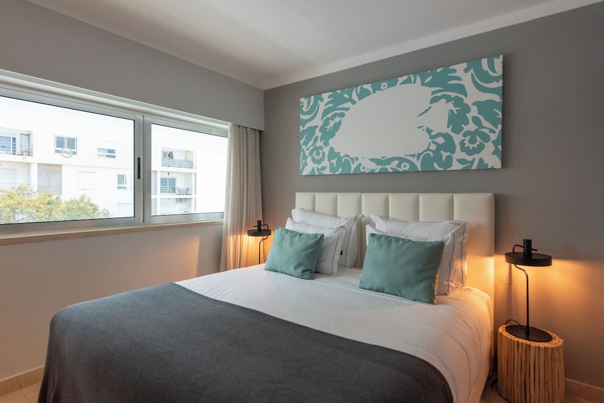 A modern hotel room with a large bed, a view of the outside, and a decorative wall piece.