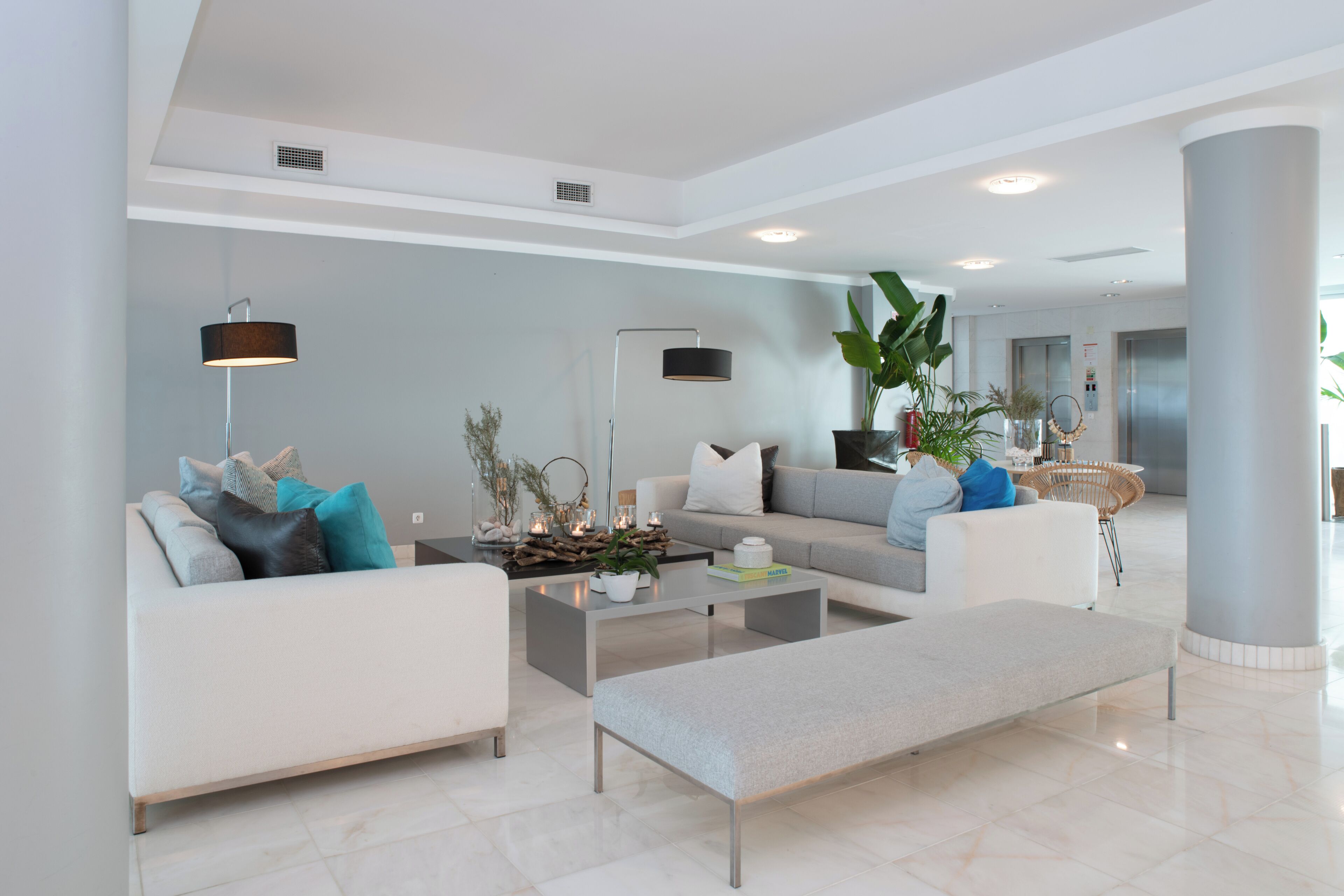A modern living room with a sofa, coffee table, and bench. There are plants and decorative items on the coffee table.
