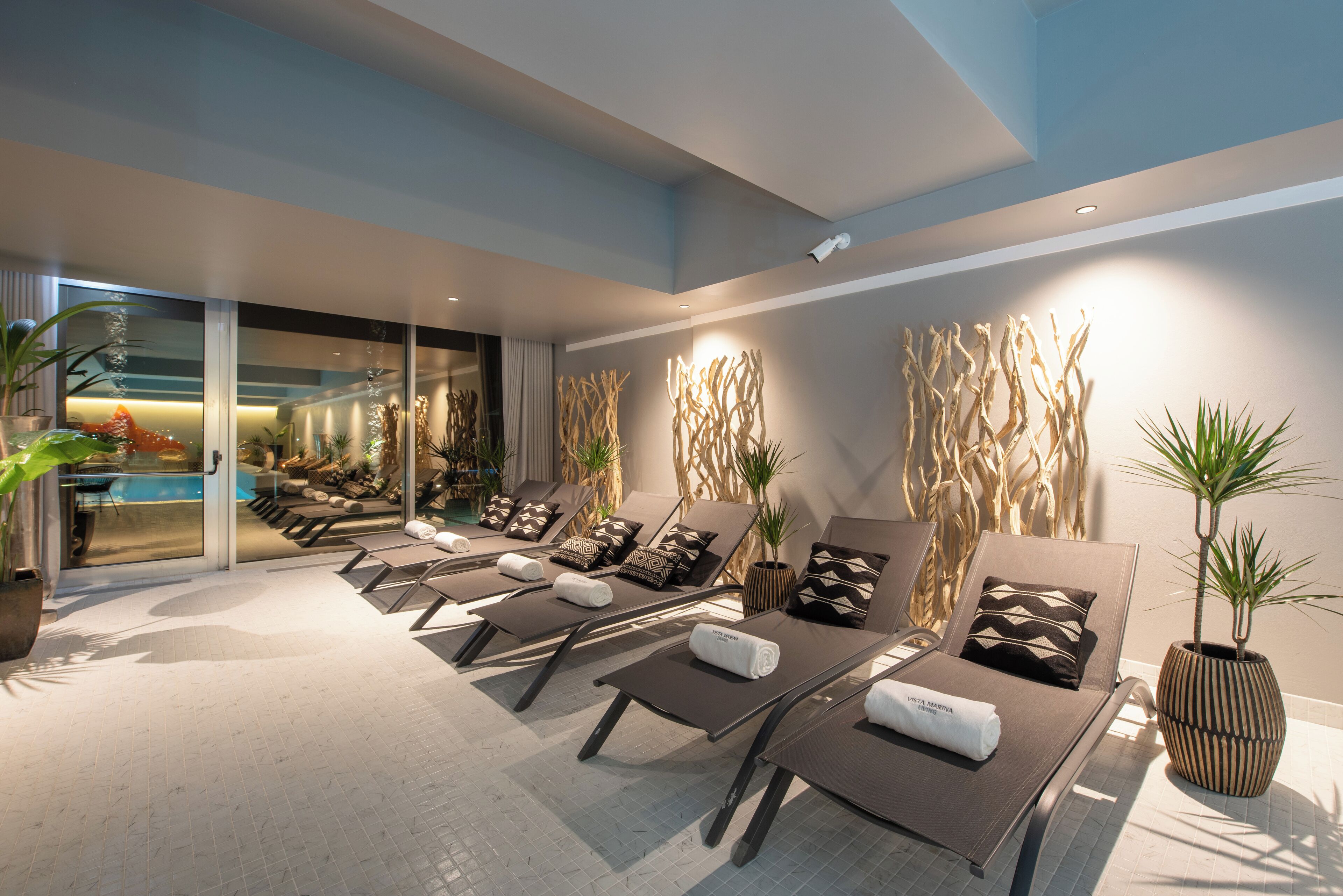 Un espace piscine intérieur moderne, doté de chaises longues, d’une piscine et offrant une vue sur l’extérieur.