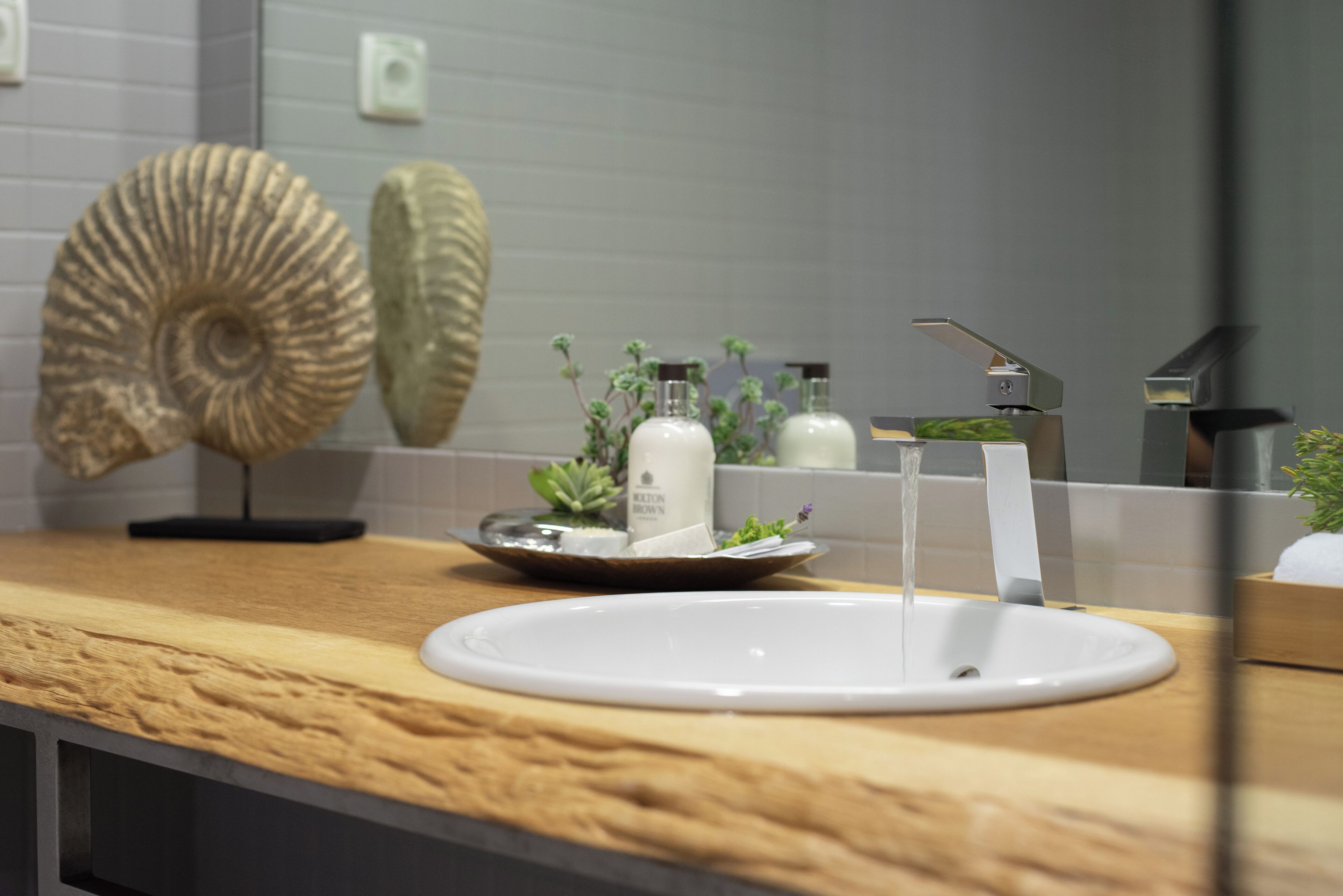 A bathroom with a wooden countertop, a white sink, and a mirror reflecting a decorative shell.