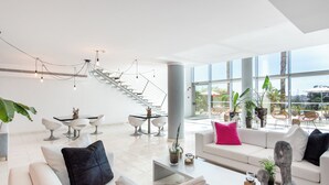 Una sala de estar moderna con una escalera, sofás blancos y un comedor con sillas blancas.