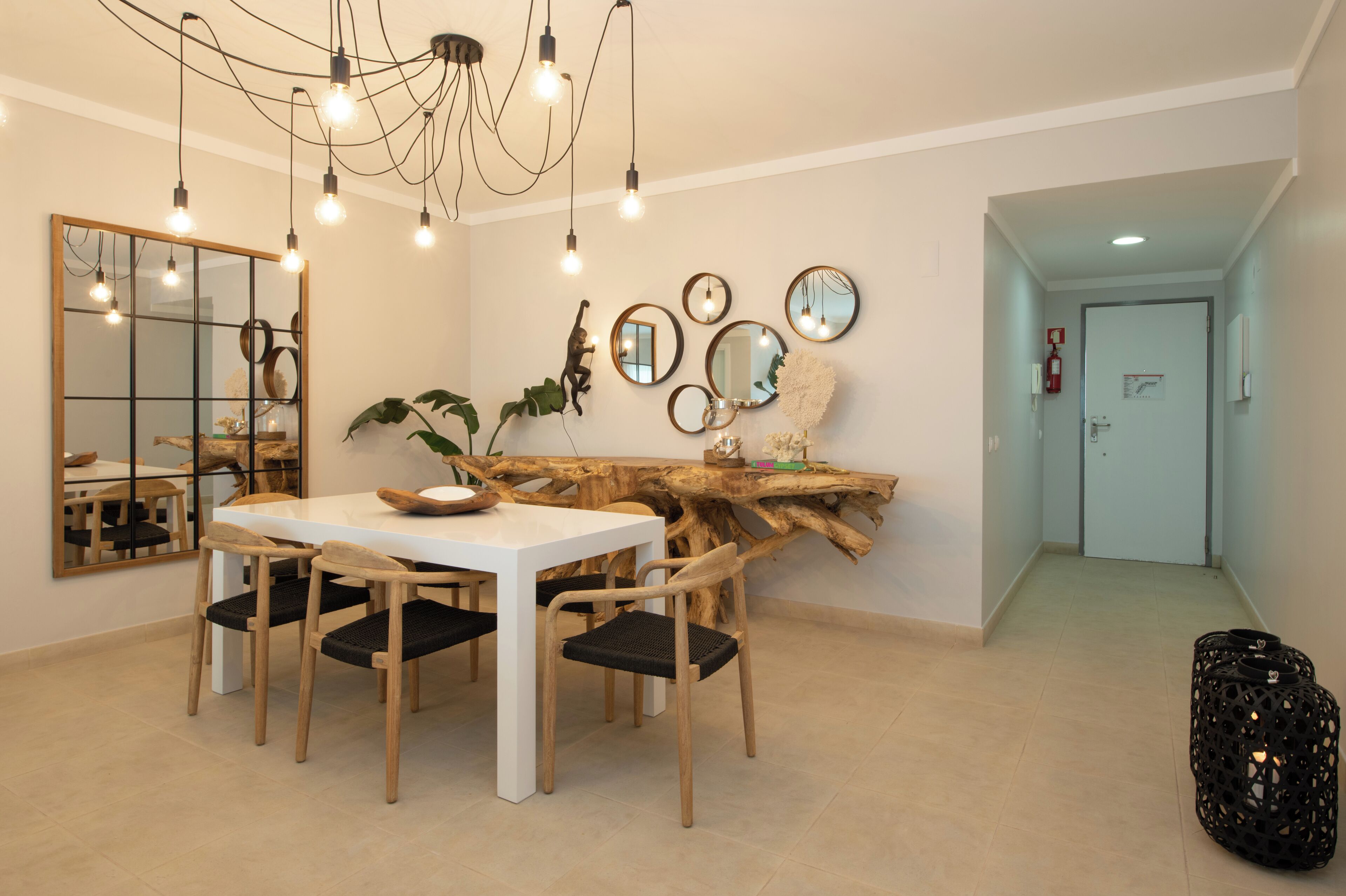 A dining area with a white table, wooden chairs, and a unique wooden art piece on the wall.
