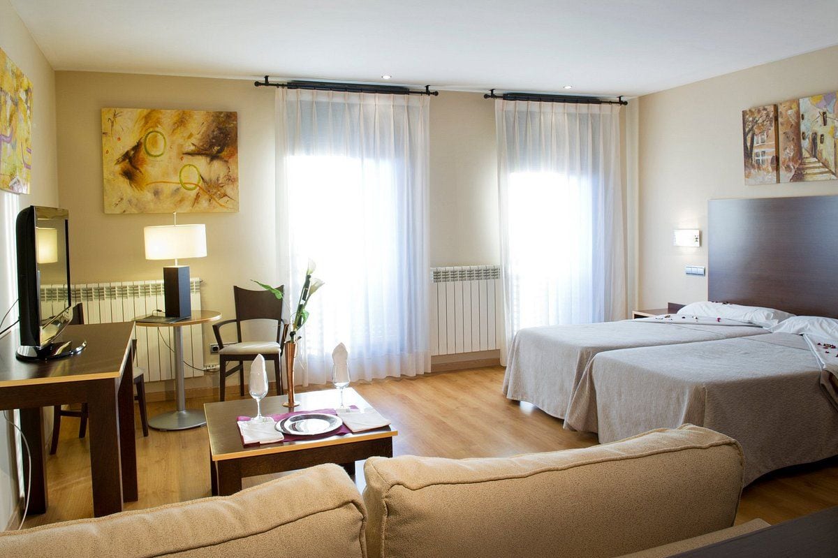 Een hotelkamer met twee bedden, een bureau met lamp, een stoel en een eettafel gedekt voor twee personen.