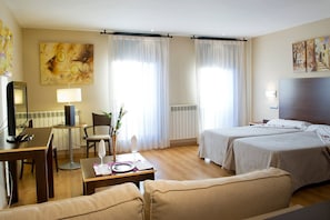 Une chambre d’hôtel avec deux lits, un bureau avec une lampe, une chaise et une table à manger dressée pour deux personnes.