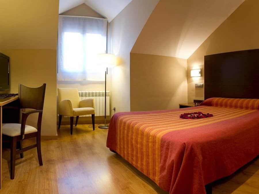Quarto de hotel com uma cama grande, uma escrivaninha com cadeira, televisão e uma luminária.